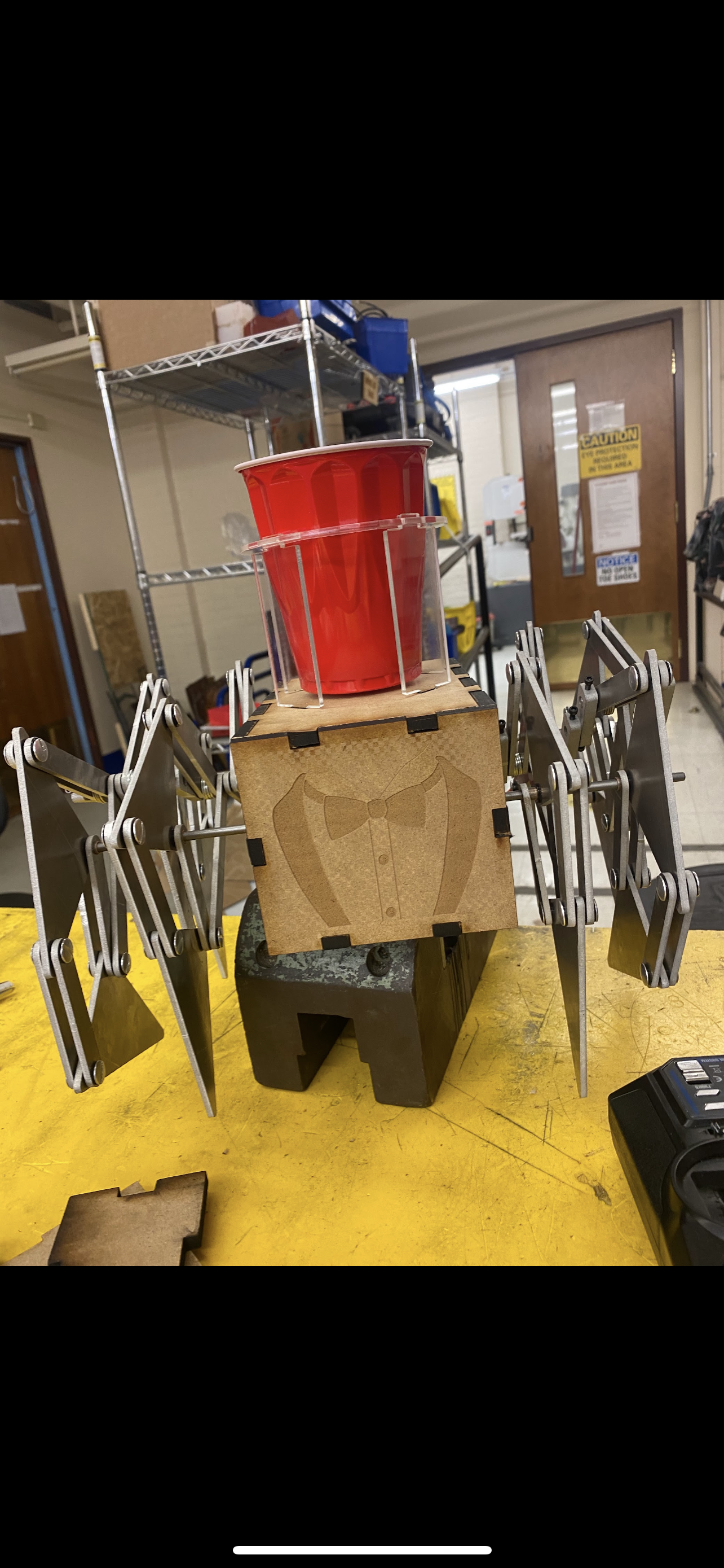 a mechanical robot with legs, an engraved tuxedo on the front, and a cupholder on top with a red solo cup in it.