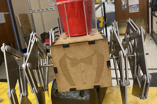 a mechanical robot with legs, an engraved tuxedo on the front, and a cupholder on top with a red solo cup in it.