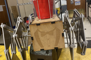 a mechanical robot with legs, an engraved tuxedo on the front, and a cupholder on top with a red solo cup in it.