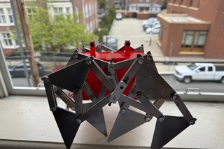 a mechanical crab with metal linkages for legs gazes out a second story window at the street below