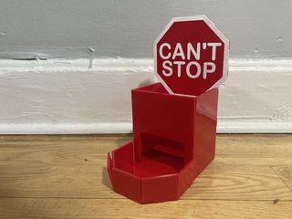 A red dice tower made from laser cut acrylic with the words "Can't Stop" painted in white on a red octagon that resembles a stop sign.