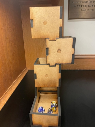 A dice tower laser cut from fiberboard.  The engravings make the dice tower appear to be a stack of six-sided dice.